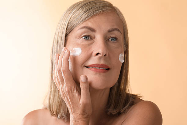 istock Senior woman applying face cream on beige background 2214779100