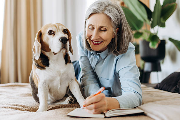 istock Senior woman lying on bed writing in notebook with beagle dog 2214783823