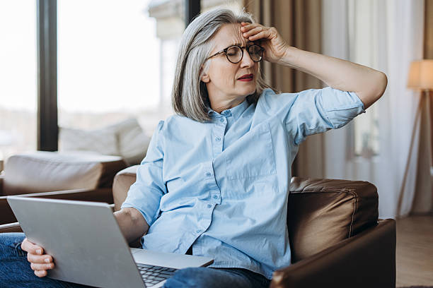 istock Stressed senior woman suffering headache while working on laptop at home 2214783884