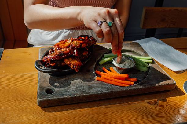 istock woman eating buffalo chicken wing plate at restaurant 2214789632