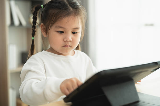 istock Young girl with braids wearing white sweater focused on tablet screen while sitting indoors, showcasing concentration and technology use in modern learning environment 2214790747