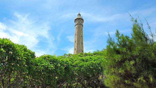 Ke Ga Lighthouse or Khe Ga Lighthouse rises above lush green trees under a bright blue sky in Binh Thuan province, Vietnam.