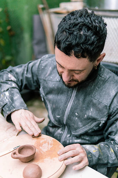 istock Potter adding clay to small cup on wooden board 2214793052