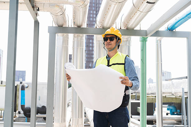 istock Engineer, Plumber, Building utilities on rooftop. Male engineer inspecting blueprint of building utilities system on rooftop of building 2214793689