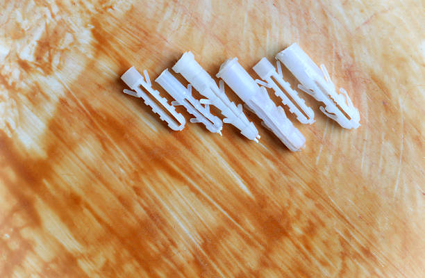 Table top view of 6 different sized white colored plastic plugs or wall anchors for screws  arranged slanted lined in a row over rough slightly dusty acrylic table background with  brown wood varnish or epoxy resin paint with messy brush strokes with copy space . Apt for construction or DIY home improvement posters, banners.