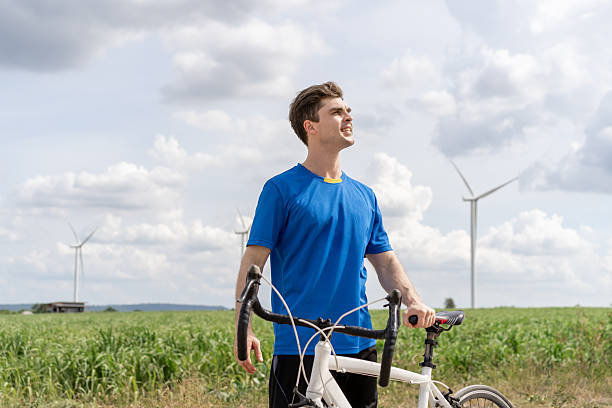 istock Caucasian man taking a break while riding bicycle at wind turbine field. Attractive athlete in sportswear exercise by cycling workout outdoors for health and wellness in rural area at windmill farm. 2214795840