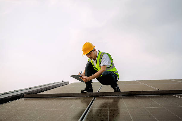 istock man in a yellow hard hat is writing on a clipboard while kneeling on a roof 2214798721