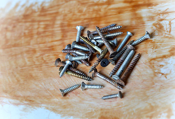 Heap or stack of several variety metal screws in different size  scattered over rough slightly dusty acrylic background with  brown wood varnish or epoxy resin paint with messy brush strokes with copy space. Apt for construction, engineering  or DIY home improvement posters, banners.