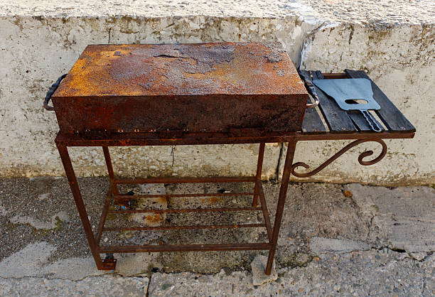 A rusty grill sits on a metal stand. The grill is covered in rust and he is old