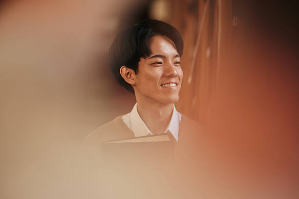 Happy Japanese male student day dreaming by the window in library. Copy space.