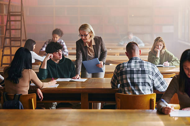 istock Senior professor assisting male student on a class in library. 2214809731