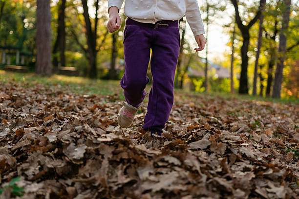 Unrecognizable little girl walking through autumn leaves in public park. Copy space