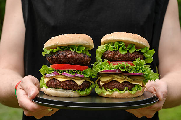 istock Waiter carrying Beautiful juicy appetizing double cheeseburgers with fresh vegetables, mega burger with cheese and lettuce and tomato 2214813739