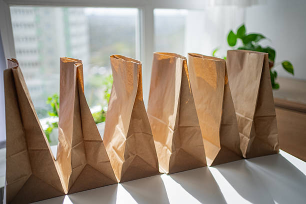 istock Brown paper bags lying open on white table beside window, natural light streaming, preparing local business delivery orders for packaging 2214814488