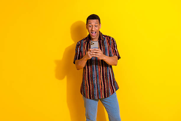istock Young man with happy expression holding smartphone on vibrant yellow background, showcasing modern lifestyle 2214816519