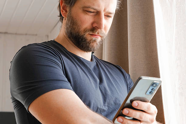 istock Man using his cellphone. Handsome guy use mobile phone at home. Male browses social networks, gaming, does shopping online, chats with friends, writes or reads messages. Close up. 2214819213