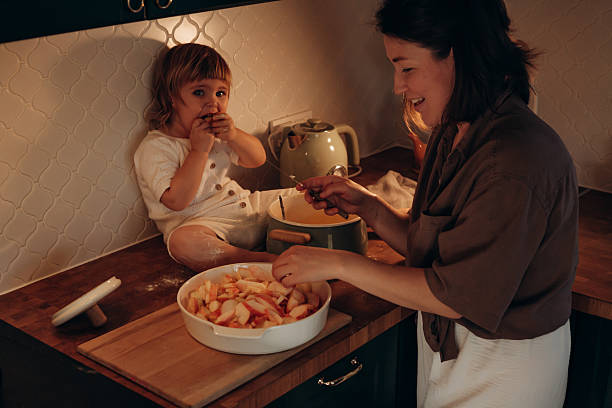 istock In a warm kitchen, a mother slices apples while her child sits on the counter, looking curious and playful. The setting is intimate and inviting, highlighting bonding moments 2214821377