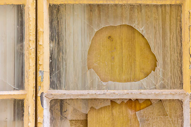 Cracked and broken glass window with visible damage, featuring rustic yellow frames and aged texture.