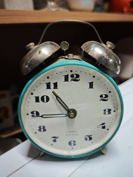 Close-up of an old-fashioned Soviet twin bell alarm clock with a teal metal frame, black numerals, and chrome bells. Photographed indoors with shallow depth of field.