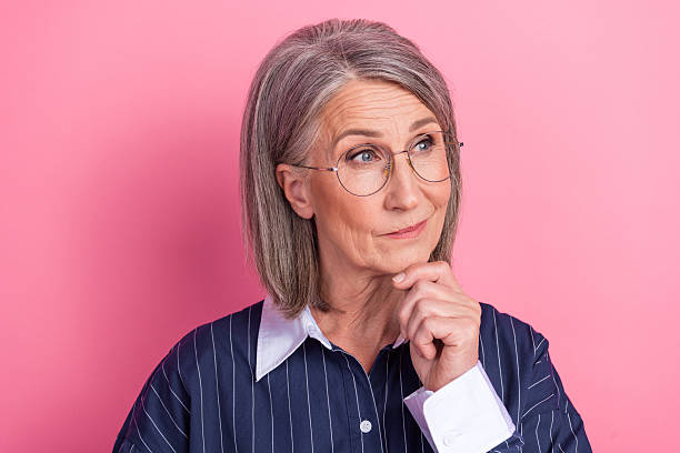 istock Mature professional female pondering with thoughtful expression against pink background wearing stylish glasses and business attire 2214828170