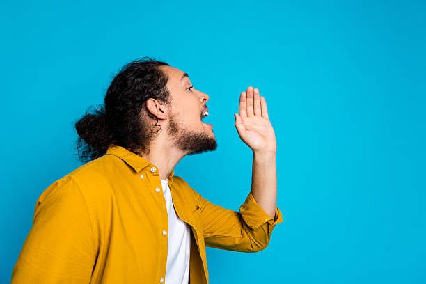 istock Man in yellow shirt gesturing while speaking against a vivid blue background 2214829037