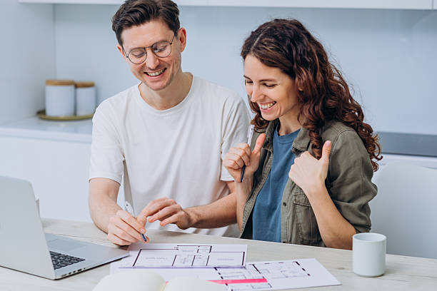 istock A joyous couple collaborates on a project, with blueprints and a laptop on the table, their laughter signifying a blend of work and pleasure. 2214829625
