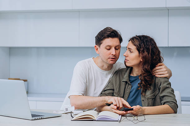 istock Young couple managing home finances using calculator and laptop at home 2214830363
