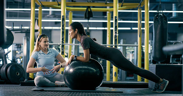 istock Stretching, personal trainer and women with ball, wellness and core stability with posture for warm up. Training, instructor and people with routine in morning, team and sportswear for balance in gym 2214831581