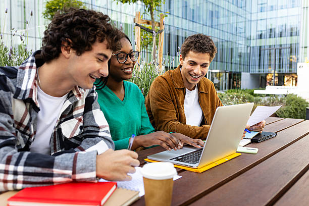 Happy diverse students working together on a project using laptop, taking notes and smiling at campus