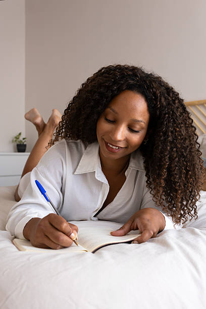 istock Young woman lying on bed writing in notebook 2214836495