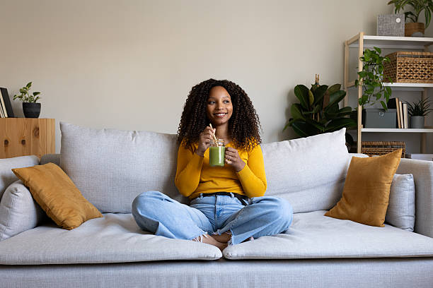 Young woman enjoying a healthy green smoothie while relaxing on her comfortable sofa at home