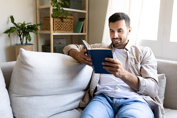 istock Young man relaxing on sofa reading a book at home 2214836655