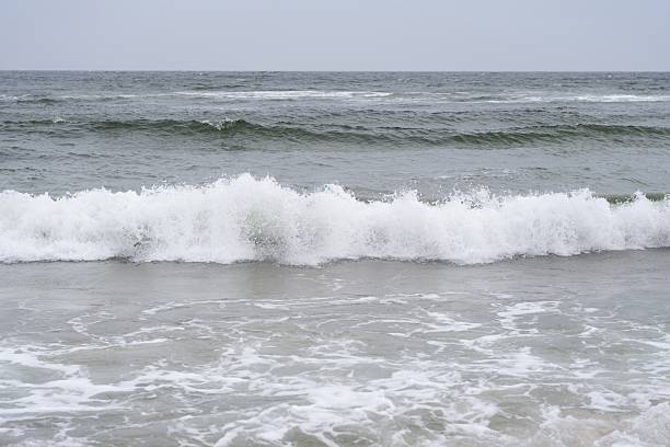 A dynamic ocean wave crashes onto the shore, creating a dramatic display of white foam and swirling water. The energy of the sea is captured in this high-resolution image, with deep blue and green hues contrasting against the frothy surf. Perfect for themes related to natures power, marine beauty, environmental awareness, and ocean conservation.