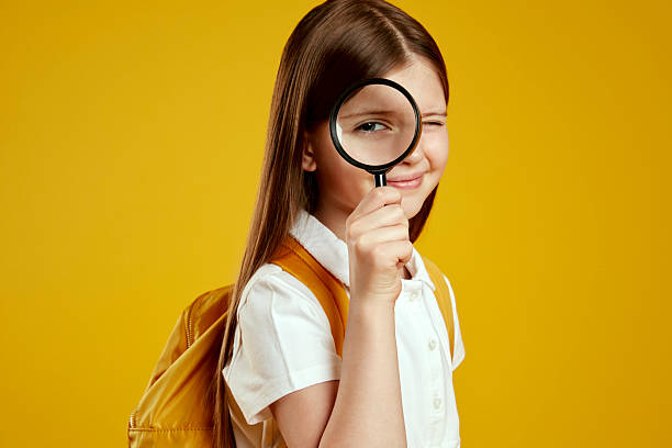 istock Curious young girl examining through magnifying glass with playful expression in classroom setting 2214841044