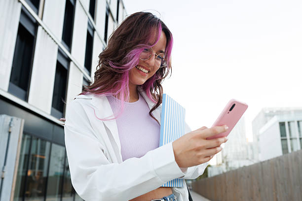 Smiling student with pink hair using smartphone in university campus