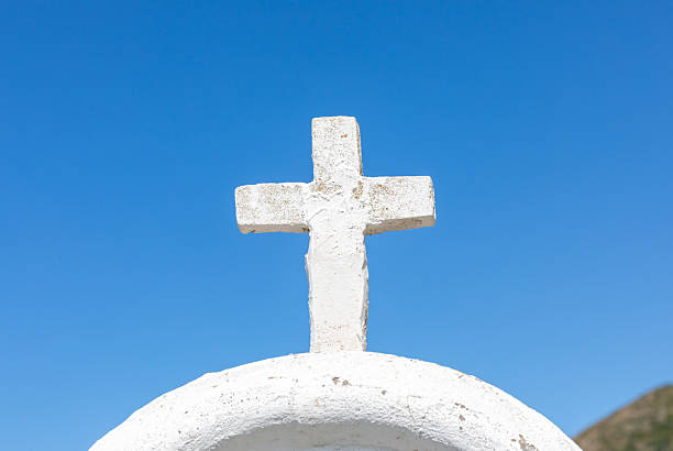 White cross rising against a white curved wall under a clear blue sky, representing themes of religion, faith, and spirituality, evoking feelings of hope and devotion
