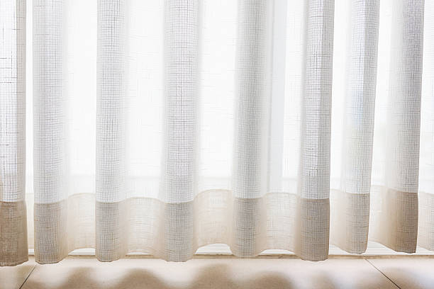 istock Dimly lit window with sheer white curtains lets in natural light. 2214846750