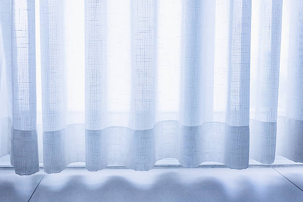 istock Dimly lit window with sheer white curtains lets in natural light. 2214846988