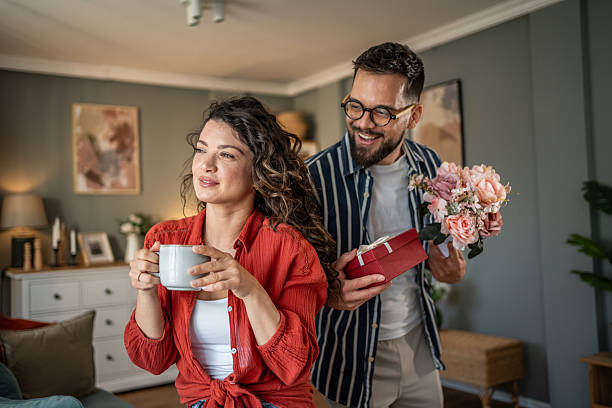 istock Man surprising his girlfriend with a gift and flowers at home 2214848327