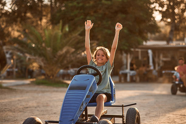 Happy child riding pedal kart on paved path in park. Young boy playing outdoor game. Joyful summer recreation and childhood fun concept. A child aged four years.