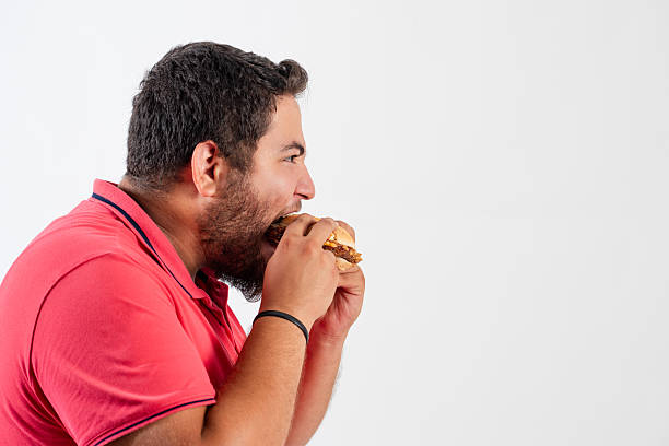 Young fat man eating fast food hamburger on white background. High quality photo