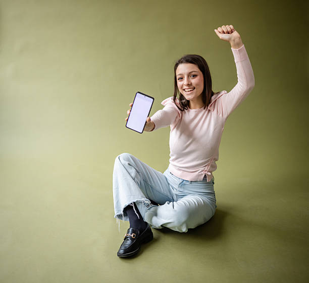 istock Young woman celebrates while sitting in a photo studio with a smartphone in hand 2214853810