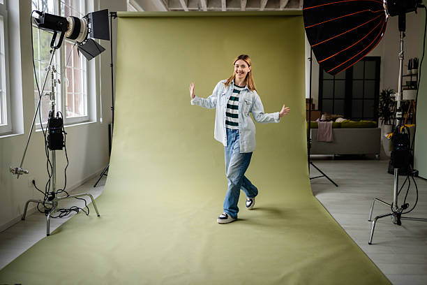 istock Young woman confidently poses in a photo studio with creative lighting setup and a green backdrop 2214854040