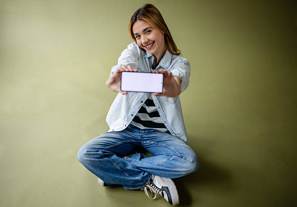 istock Young woman poses casually in a studio setting while holding a smartphone, showcasing her relaxed confidence and creativity 2214855268