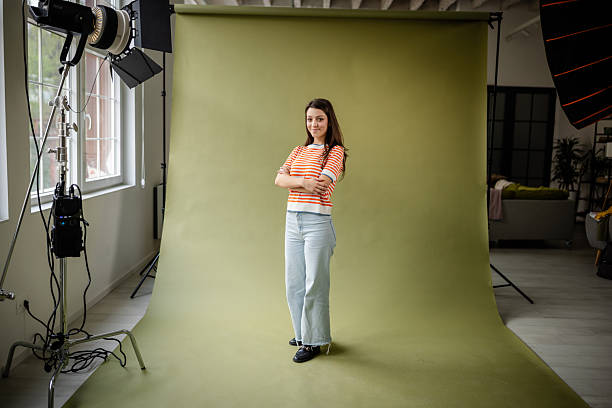 istock Young woman posing confidently in a photo studio with green backdrop and professional lighting equipment 2214856779