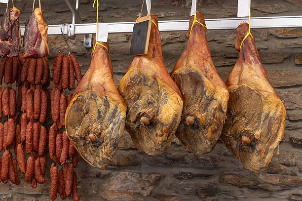 A variety of meats, such as ham and sausages, are hanging on a rack