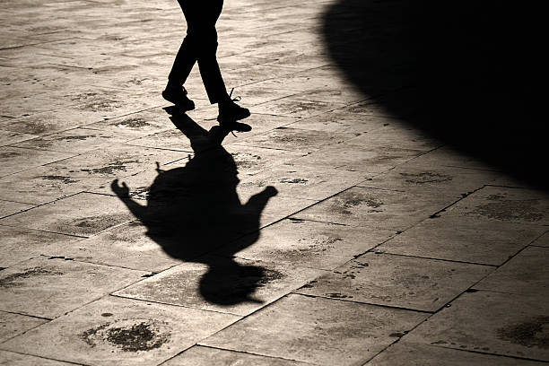 istock Silhouette of a walking person with a gesturing hand, casting a dramatic shadow over the textured stone tiles. 2214860169