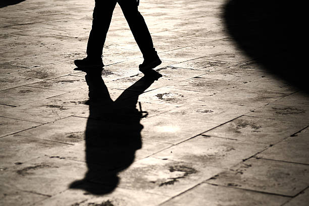 istock One person walking alone on sunlit tiles with a sharp silhouette and elongated shadow stretching across the ground. 2214860175