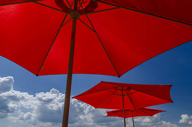 istock Bright Red Sun Umbrellas Against Blue Sky with Fluffy Clouds on a Hot Sunny Summer Day 2214868739