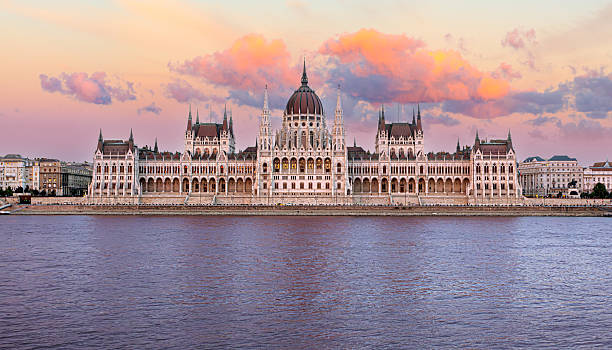 Hungarian parliament building reflecting on danube river at sunset with colorful clouds